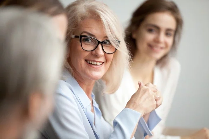 older-lady-with-glasses-smiling-coworkers-1 Woman smiling within a group